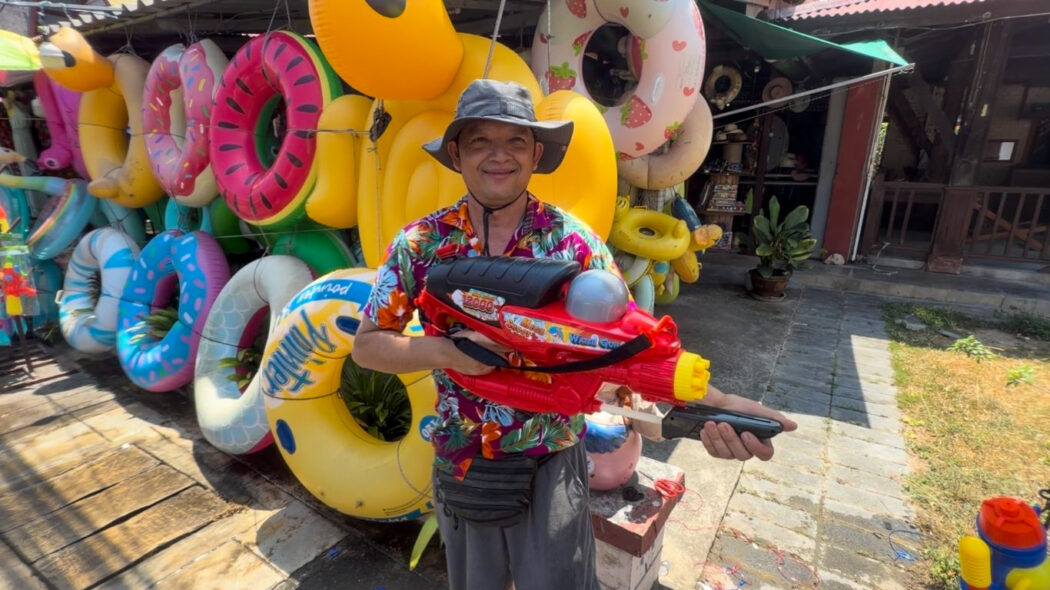 Smiling Thai man holding a large water gun at a Songkran festival shop in Koh Samui, Thailand 2026