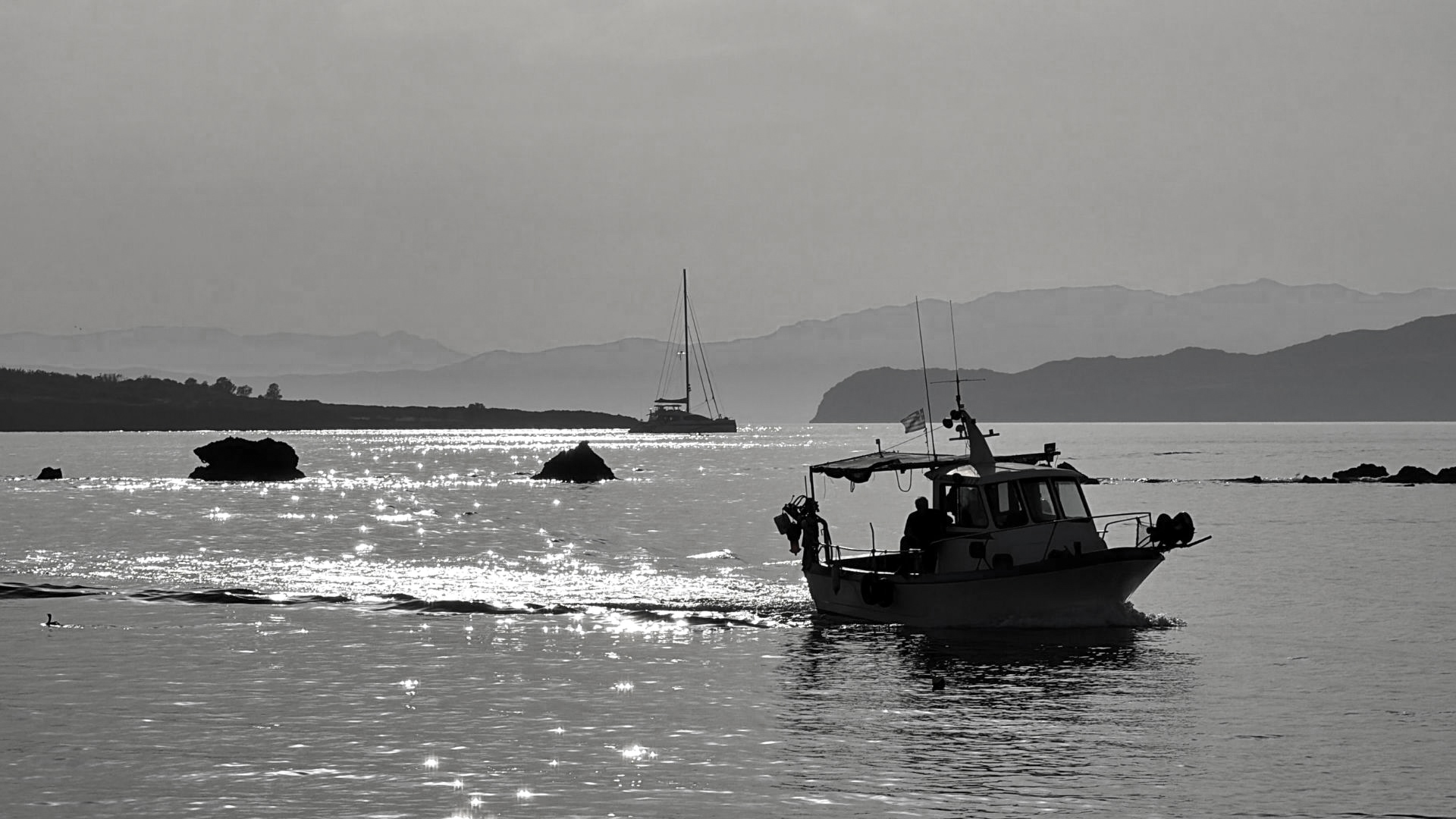 Black and white photo of a fishing boat at sunset on the sea in Crete