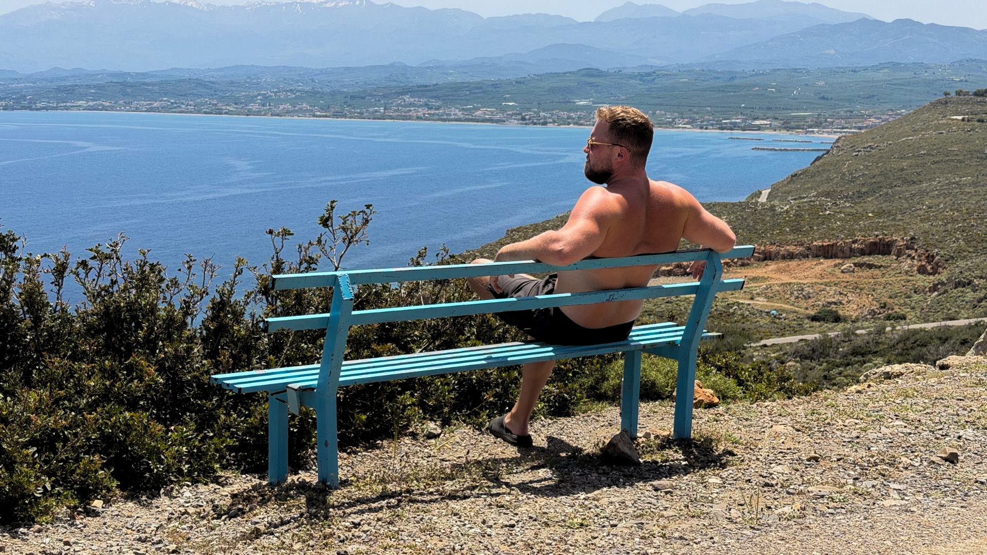 Man sitting on a blue bench at a scenic mountain viewpoint overlooking the sea in Crete
